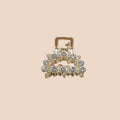 Gold hair clip with gemstones held by a hand against a plain background