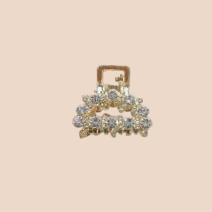 Gold hair clip with gemstones held by a hand against a plain background