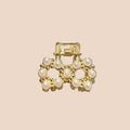 Gold hair clip with pearl-like stones held by a hand against a neutral background