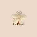 Floral hair clip with pearls held between fingers against a neutral background