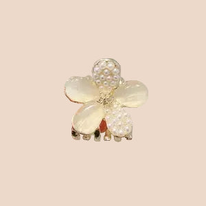 Floral hair clip with pearls held between fingers against a neutral background